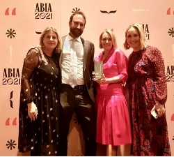Three women and one man pose on the ABIA red carpet. The woman standing second from the right wears a hot pink dress and holds an ABIA award